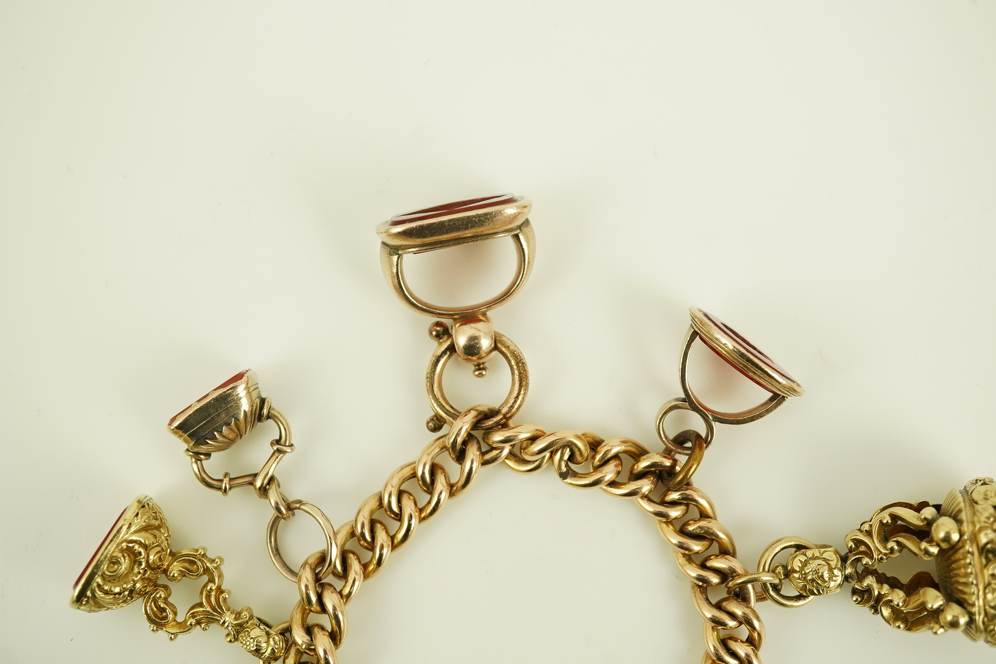An Edwardian 15ct gold curb link charm bracelet with heart shaped padlock clasp, hung with six assorted gold overlaid and carnelian set fob seals